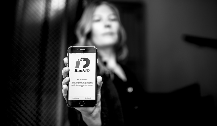 Hand som håller fram en mobiltelefon som visar vy av BankID-appen.